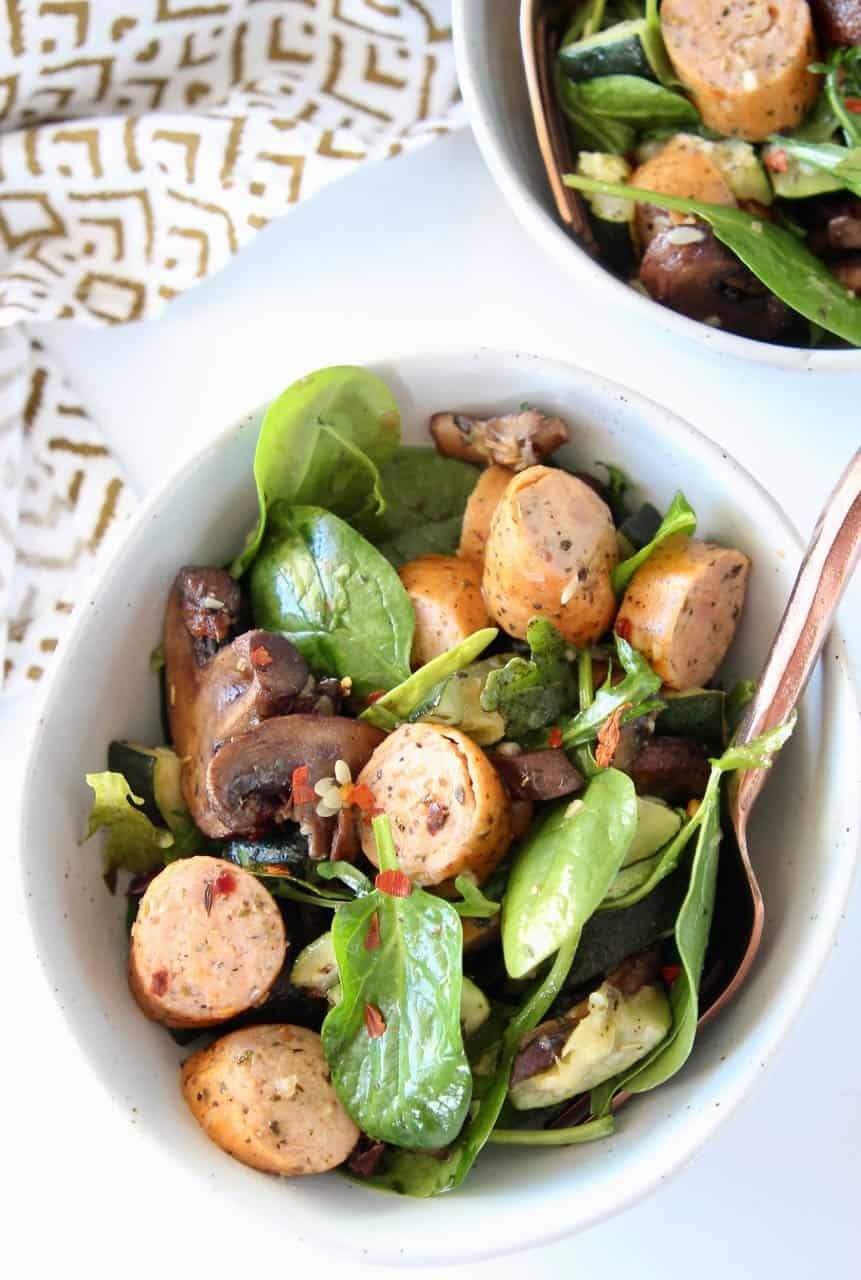 Spinach leaves, sliced sausage, and zucchini in a white bowl