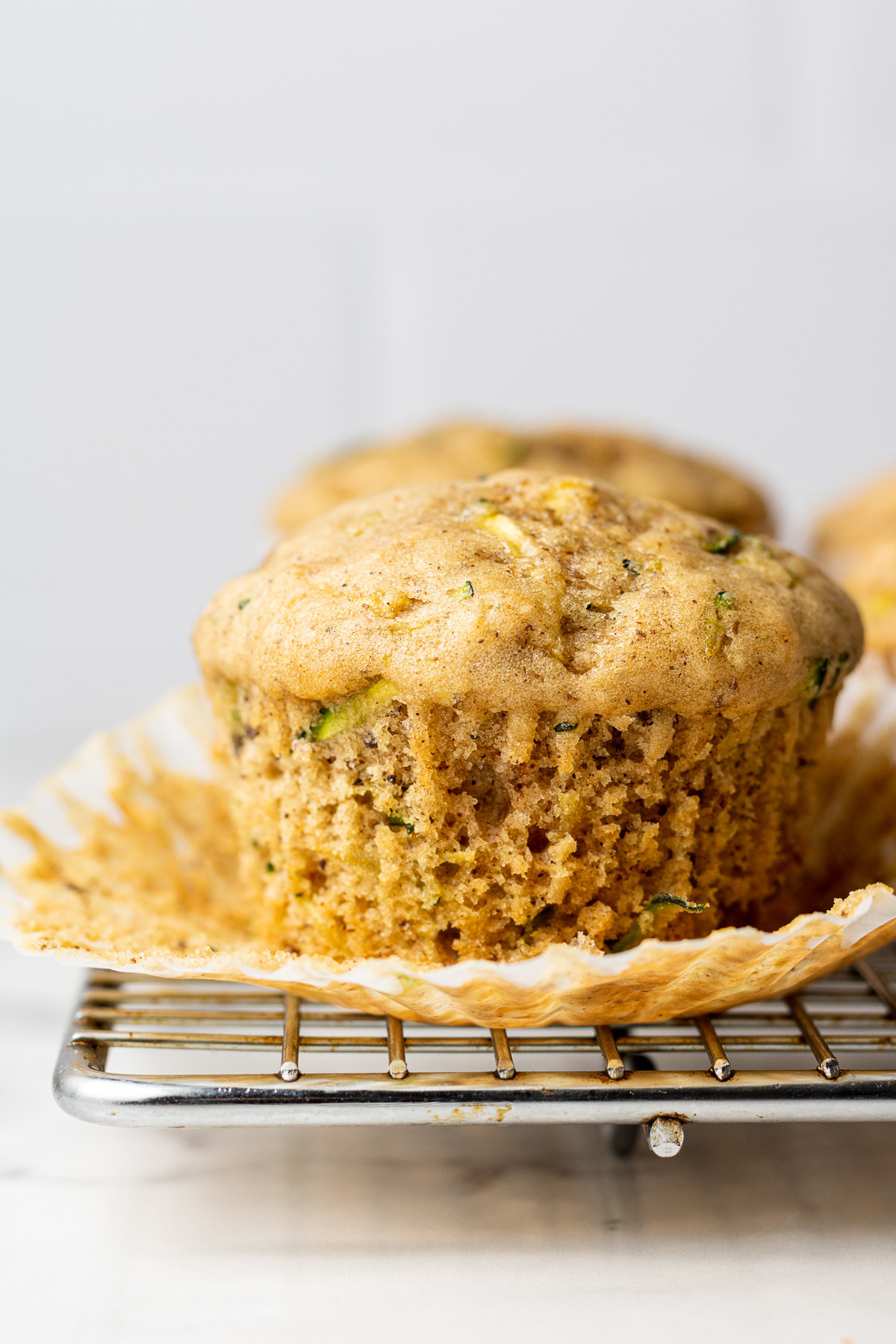 Unwrapped zucchini muffin on a metal cooling rack.