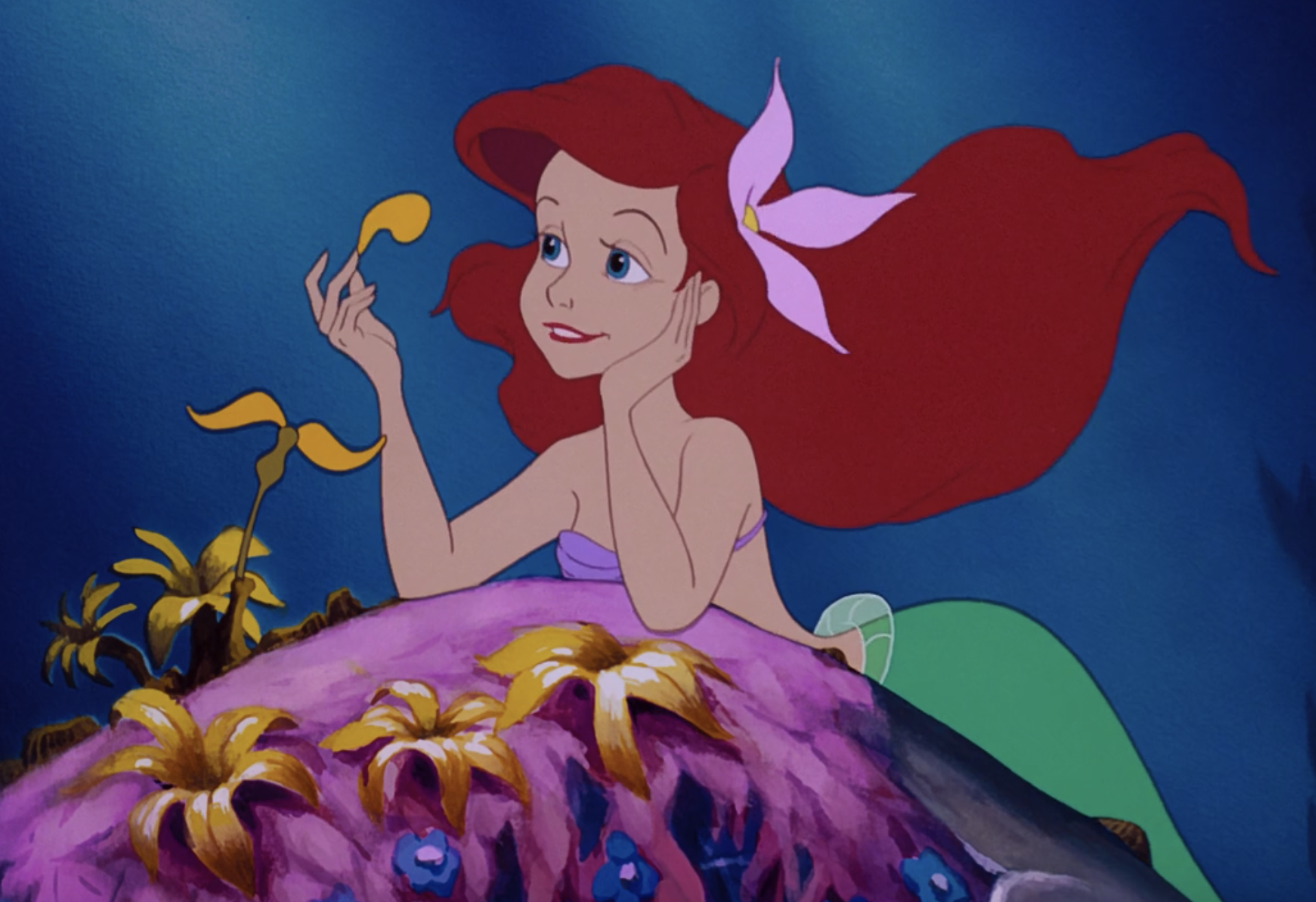 Ariel leans against a rock, picking some seaweed while resting a hand on her chin