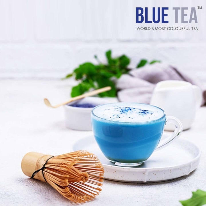 A cup of blue tea with foam on top.