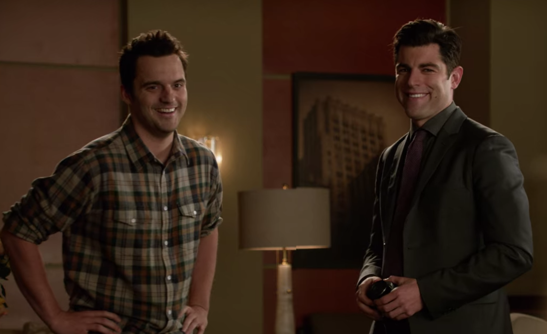 Nick Miller, smiling with hands on hips, wears a brown, red, and green checkered flannel shirt while Schmidt wears a dark-gray suit