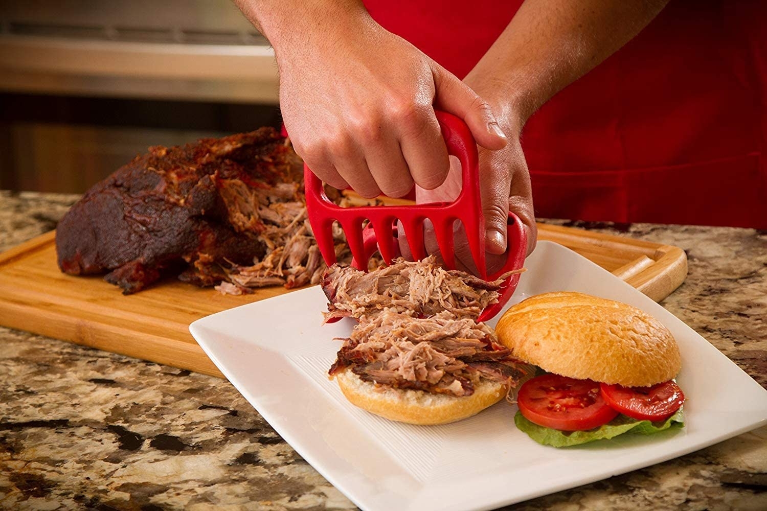 Hands use two red shredding claws to cut up pulled pork on a plate