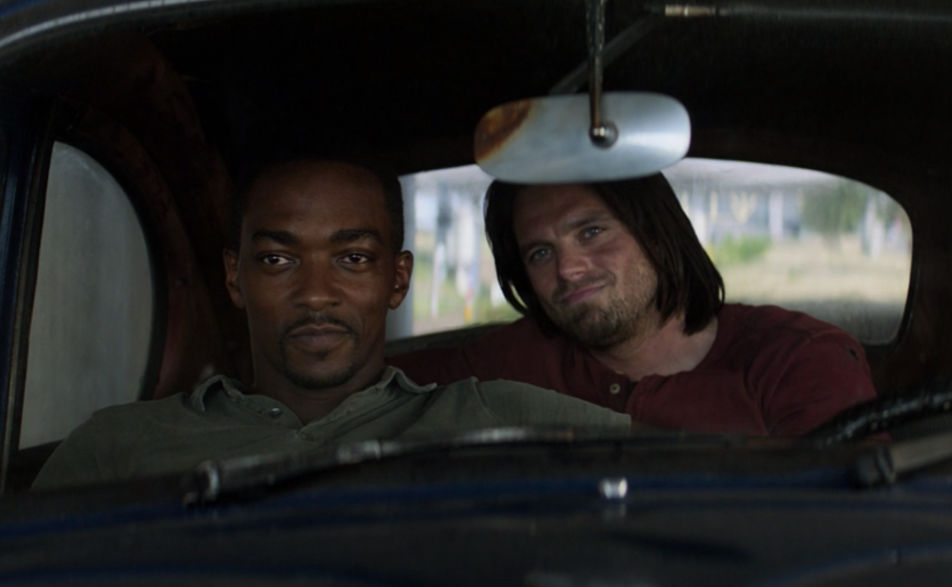 Sam Wilson smiles as he sits in the driver&#x27;s seat of a car while Bucky Barnes sits behind him, smirking.