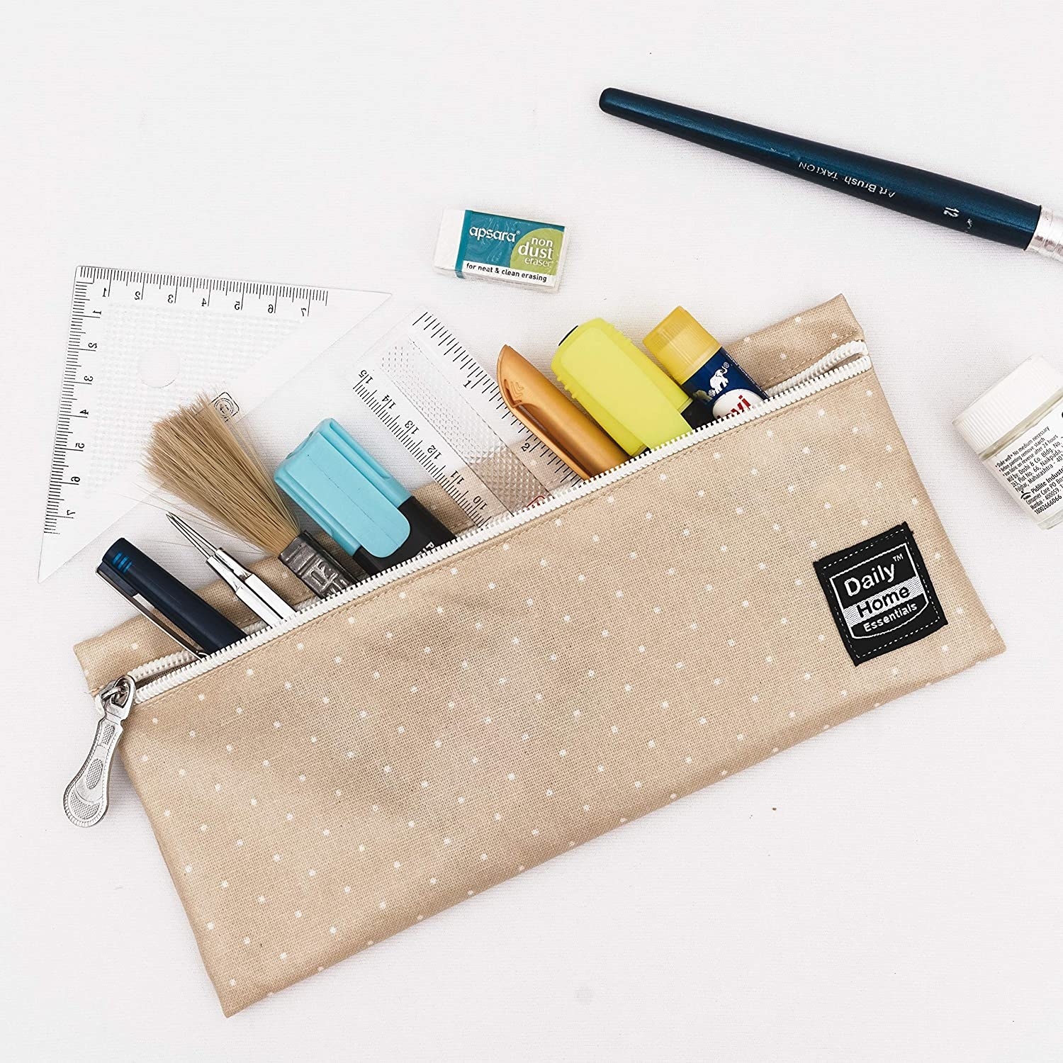 A beige pencil pouch with tiny white polka dots on it. It&#x27;s holding various stationery products like a ruler, pen, highlighter, glue stick, etc.