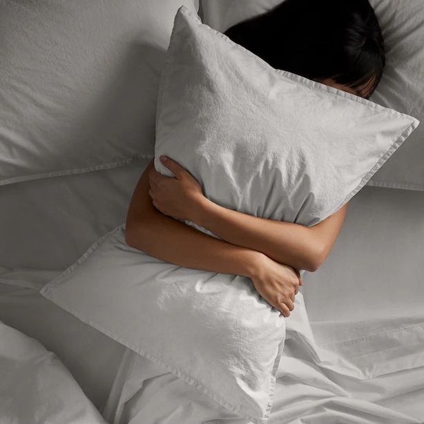 A person lying on a bed hugging a pillow