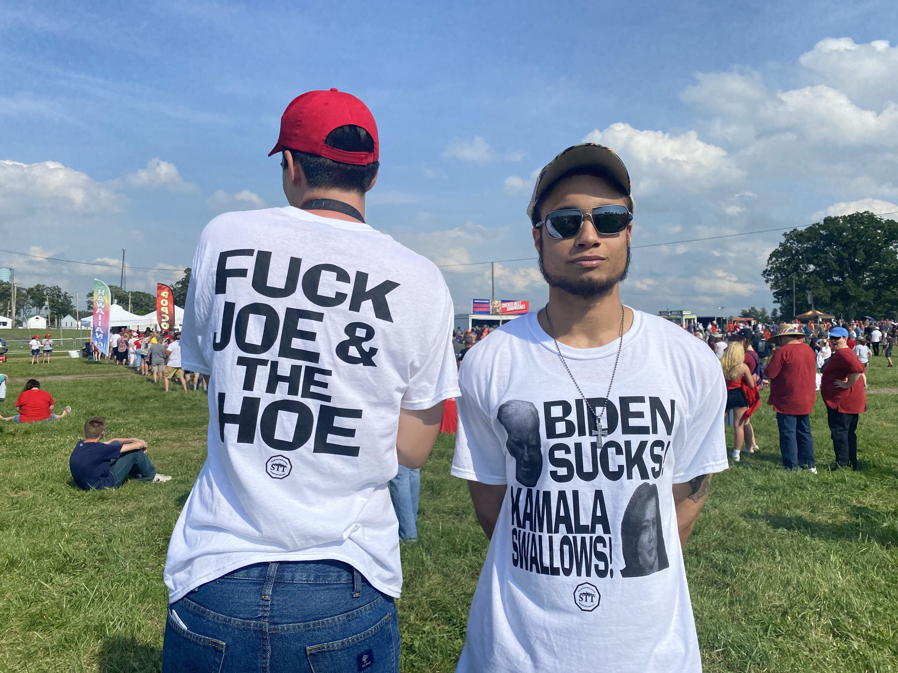 Two people wearing the same T-shirt show “Biden Sucks Kamala Swallows!” on the front and “Fuck Joe & the Hoe” on the back