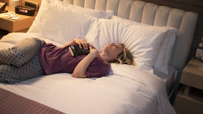 Kaley holding a book as she lays on a bed in a scene from The Flight Attendant
