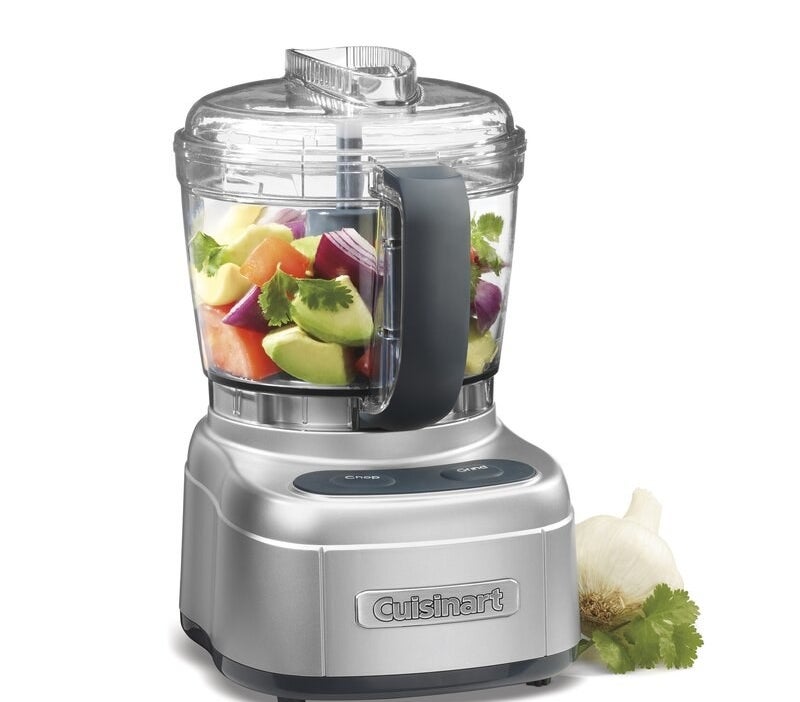 the food processor with vegetable in the basket and a garlic clove next to it