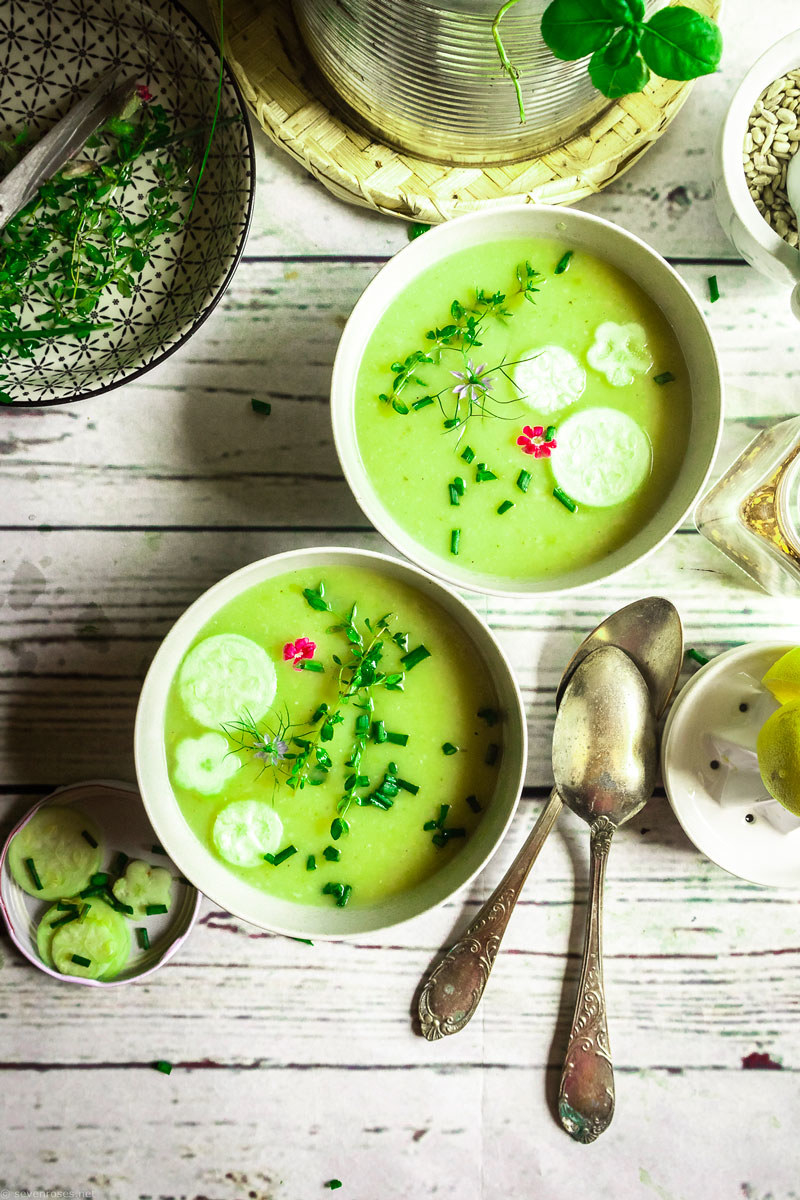 White bowls filled with bright green soup topped with herbs on a wooden surface next to spoons