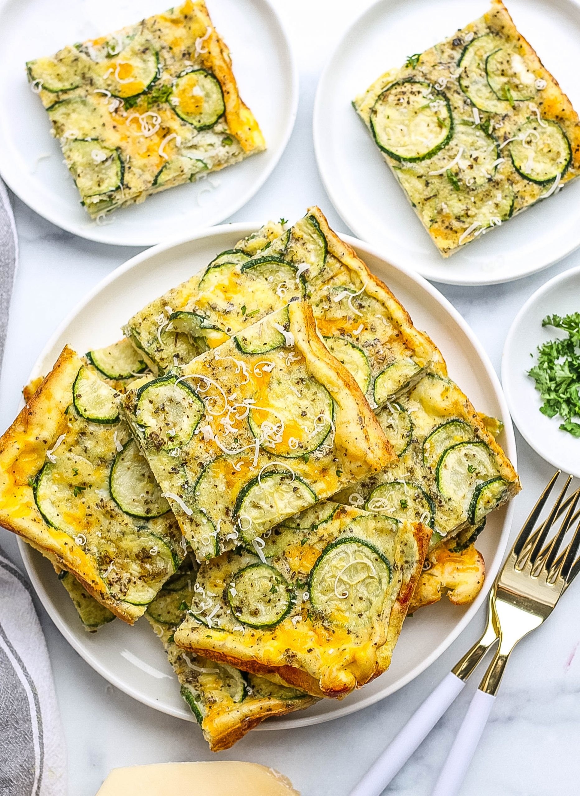 Zucchini frittata squares on a white plate next to forks