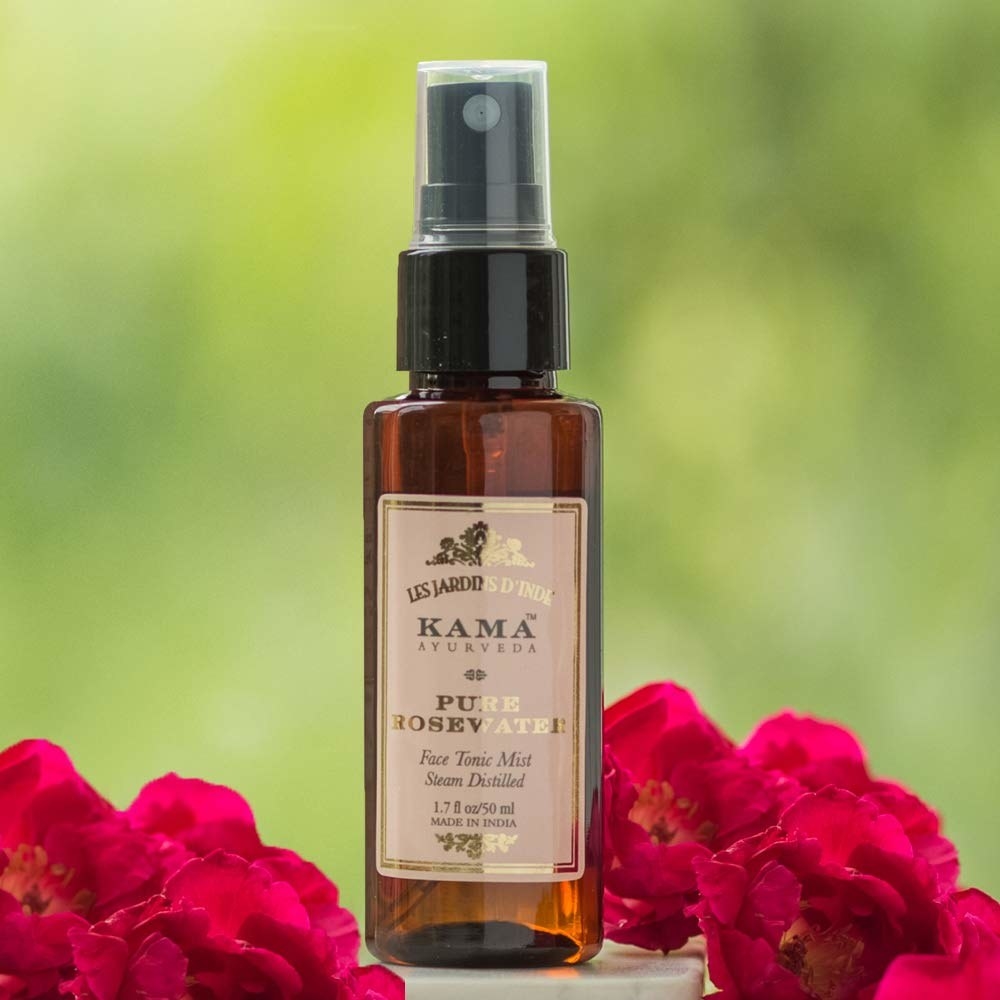 A bottle of Kama Ayurveda rose water with roses kept on the side of the bottle.