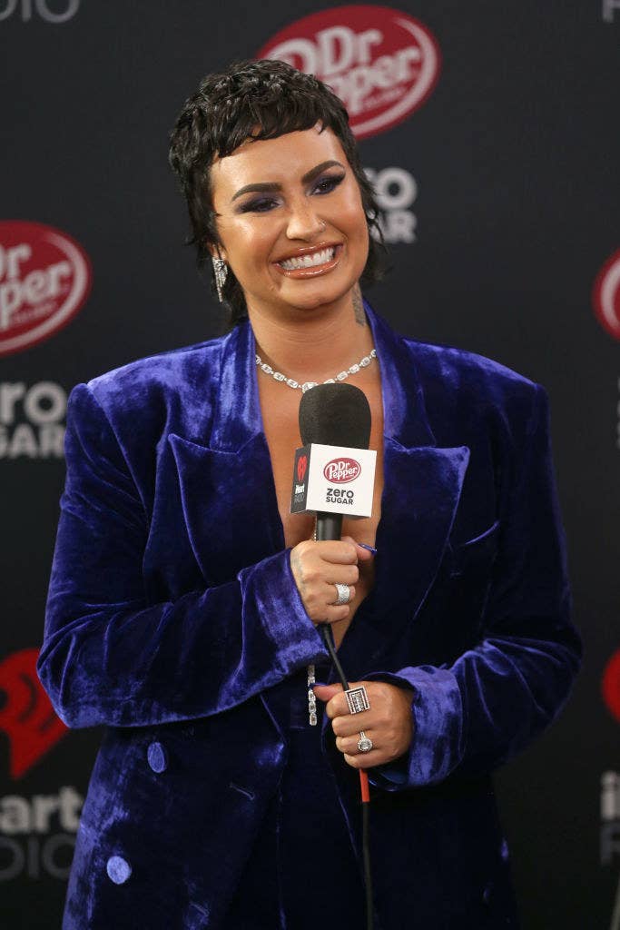 Demi Lovato smiles while being interviewed wearing a blue velvet blazer.