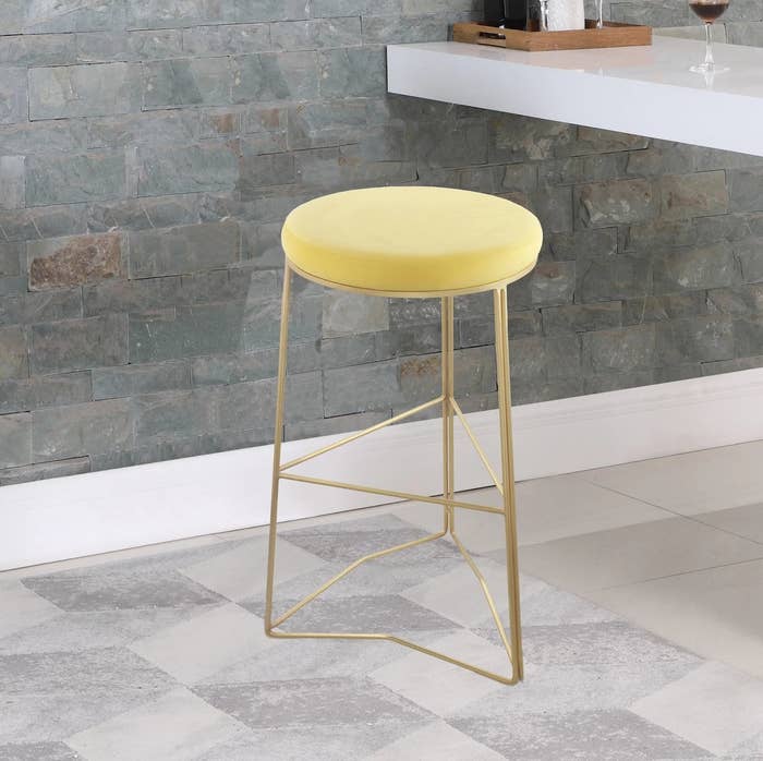The round bar stool with a gold base and yellow cushioned seat in a kitchen