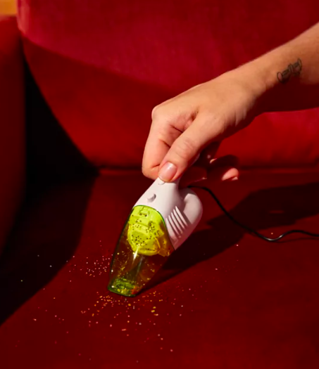 A person using the mini vacuum to clean up crumbs on a sofa