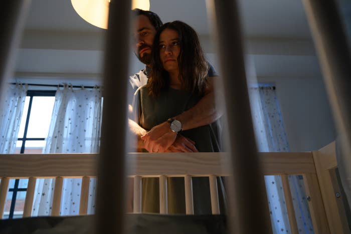 Adrian hugging Lucy from behind as they stand by a crib