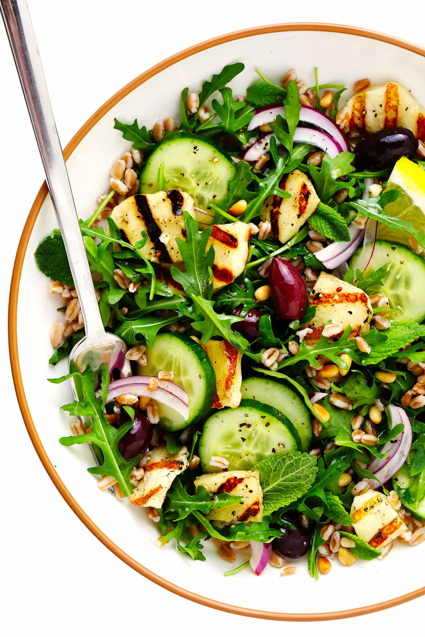 White bowl filled with halloumi salad containing sliced cucumber, sliced onions, grilled halloumi, and arugula.