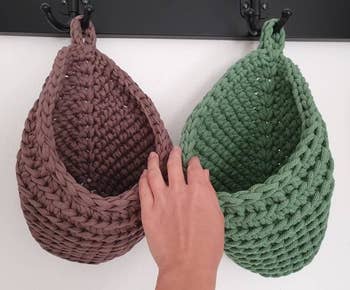 a hand holding open two of the knit hanging baskets 