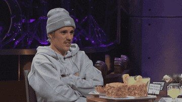 GIF of Justin sitting at a table with his hands folded and looking disgusted
