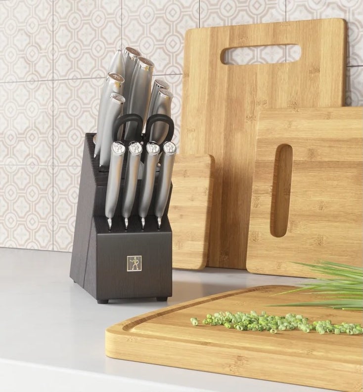 The stainless steel knife set in a black knife block on a kitchen counter next to a bamboo cutting board