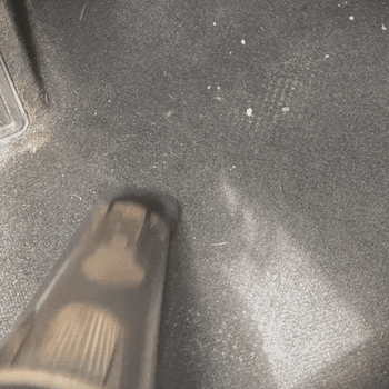 The vacuum sucking dirt and rocks from a driver's seat floor in a car