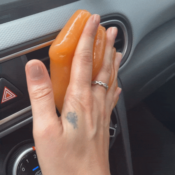 A person rolling an orange putty over a car AC vent