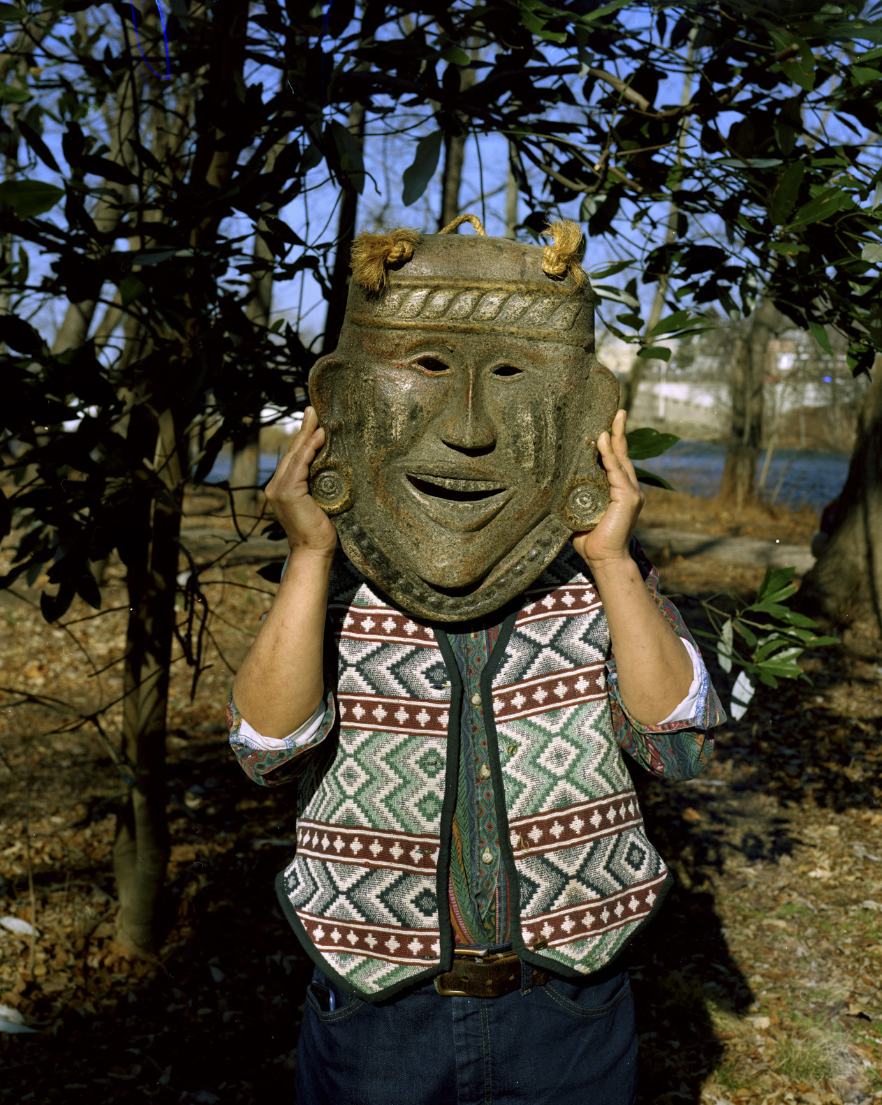 A man holding up a large replica of an Indigenous clay mask to this face