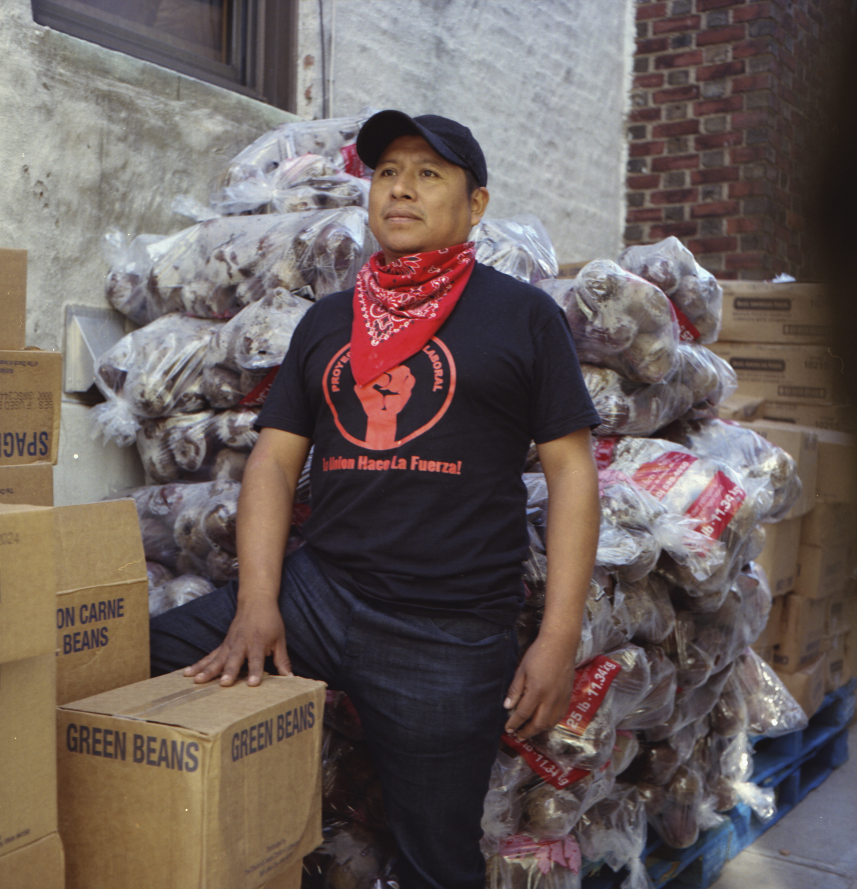 A man with a bandana around his neck in front of a box of green beans and piles of food