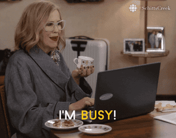 gif of moira rose from the series schitts creek siting behind a computer holding a cup of tea saying I&#x27;m busy