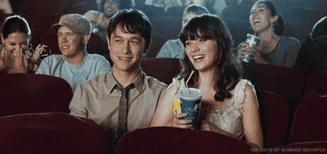 Joseph Gordon-Levitt next to laughing Zooey Deschanel at the movies; people laughing in seats behind them