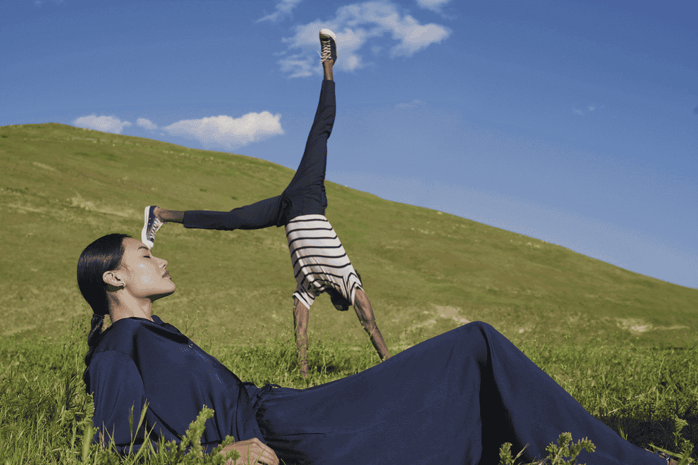 A person doing a cartwheel behind a person lying on the grass in a dress