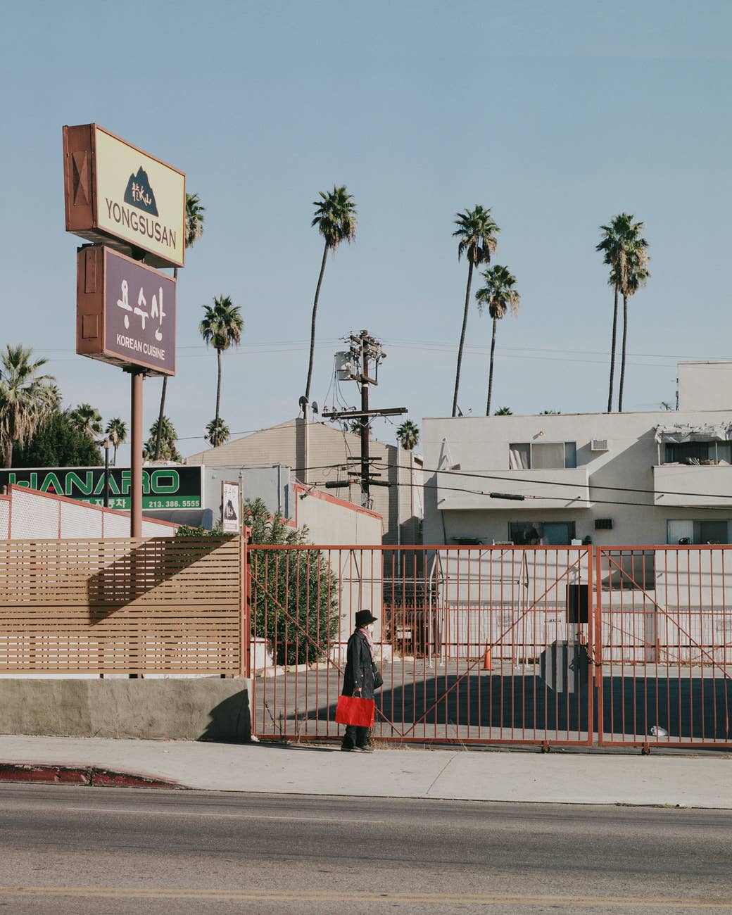 A woman with a red bag walks by a gate in Koreatown 