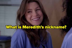 Meredith Grey smiles as she shrugs one of her shoulders.