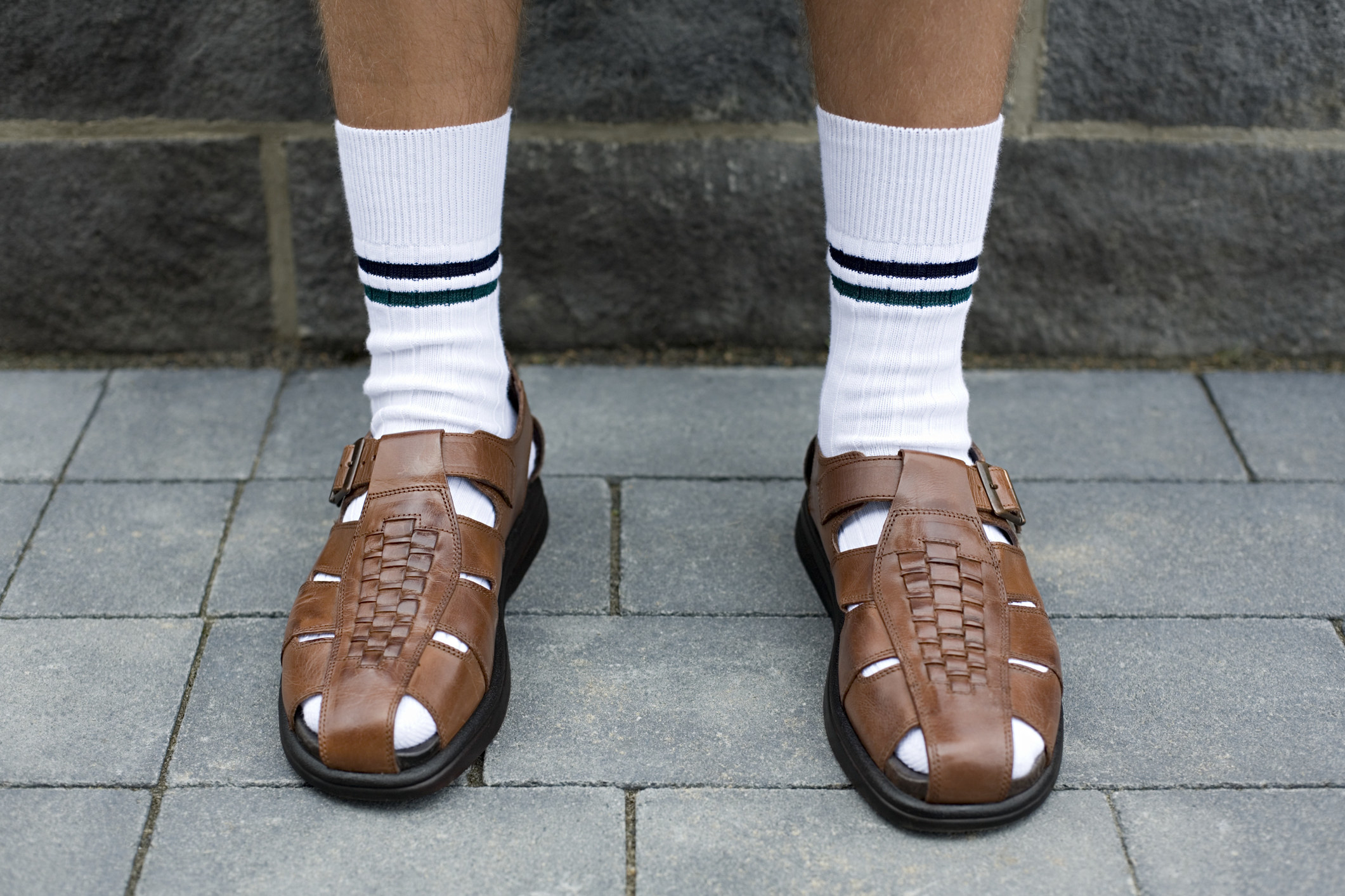 A man&#x27;s legs from mid-calf down, wearing high white socks with two stripes and brown leather sandals