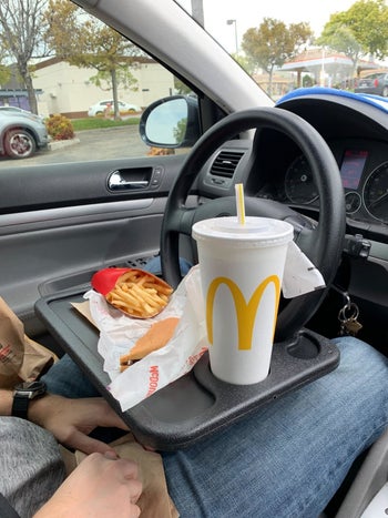 A reviewer photo of a person sitting in a car with a tray attached to the steering wheel