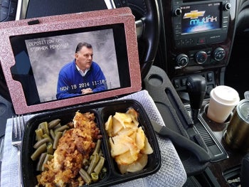 A reviewer photo of an iPad and food on a tray attached to the steering wheel of a car