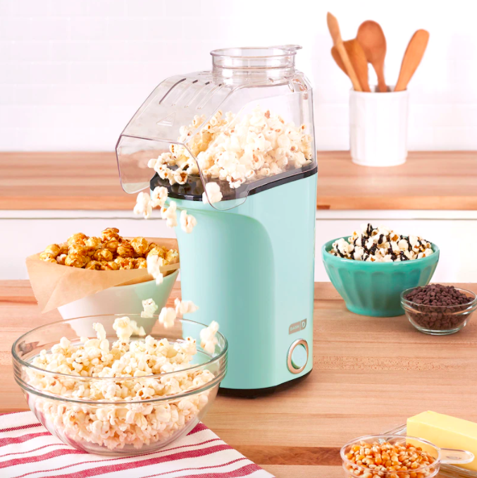 A popcorn maker dropping freshly popped kernels into a glass bowl