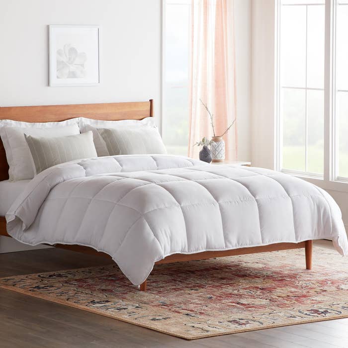 The white comforter with large box-stitch designs is in a light and airy room