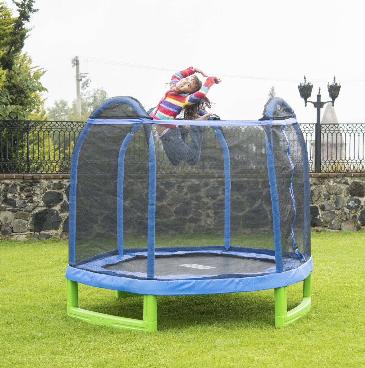 The trampoline has a blue frame and black netting and green sturdy bottom with a child jumping at the top