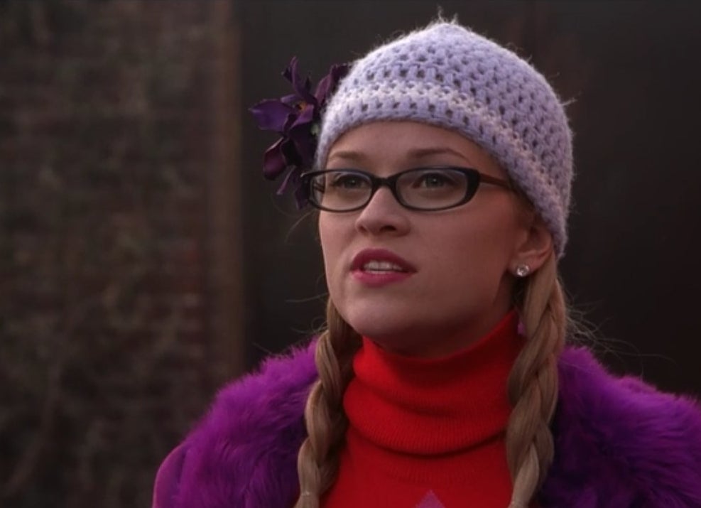 Elle wears a turtleneck, fur coat, and beanie, with glasses