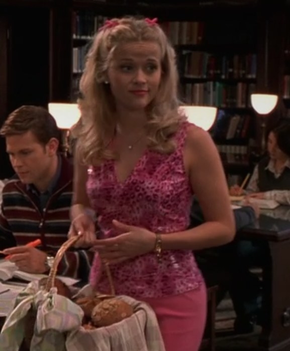 Elle wears a pink top and pants, with pink bows in her hair, and holds a basket of bread