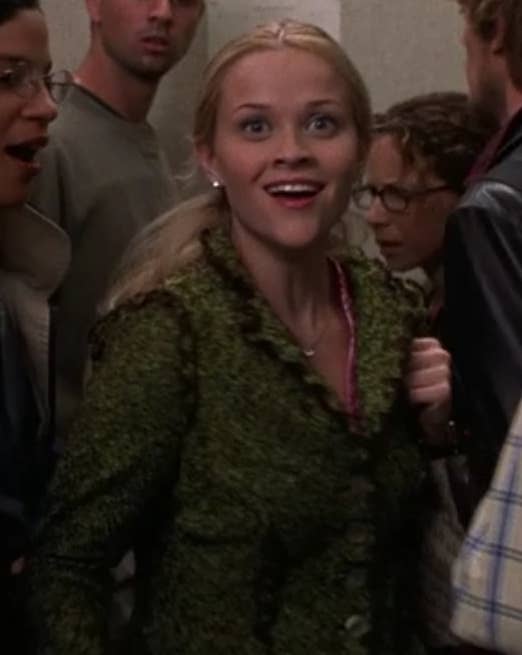 Elle wears a green jacket buttoned up and looks excited