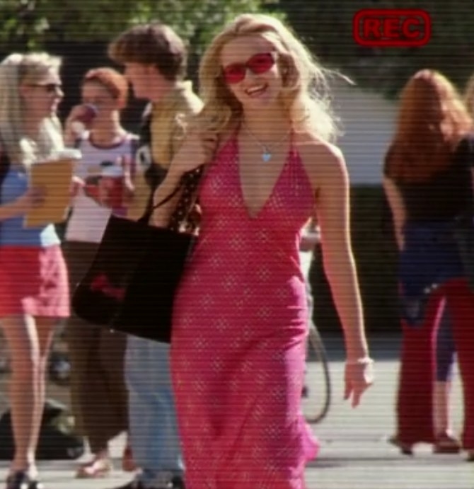 Elle wears a pink halter dress and pink tinted glasses