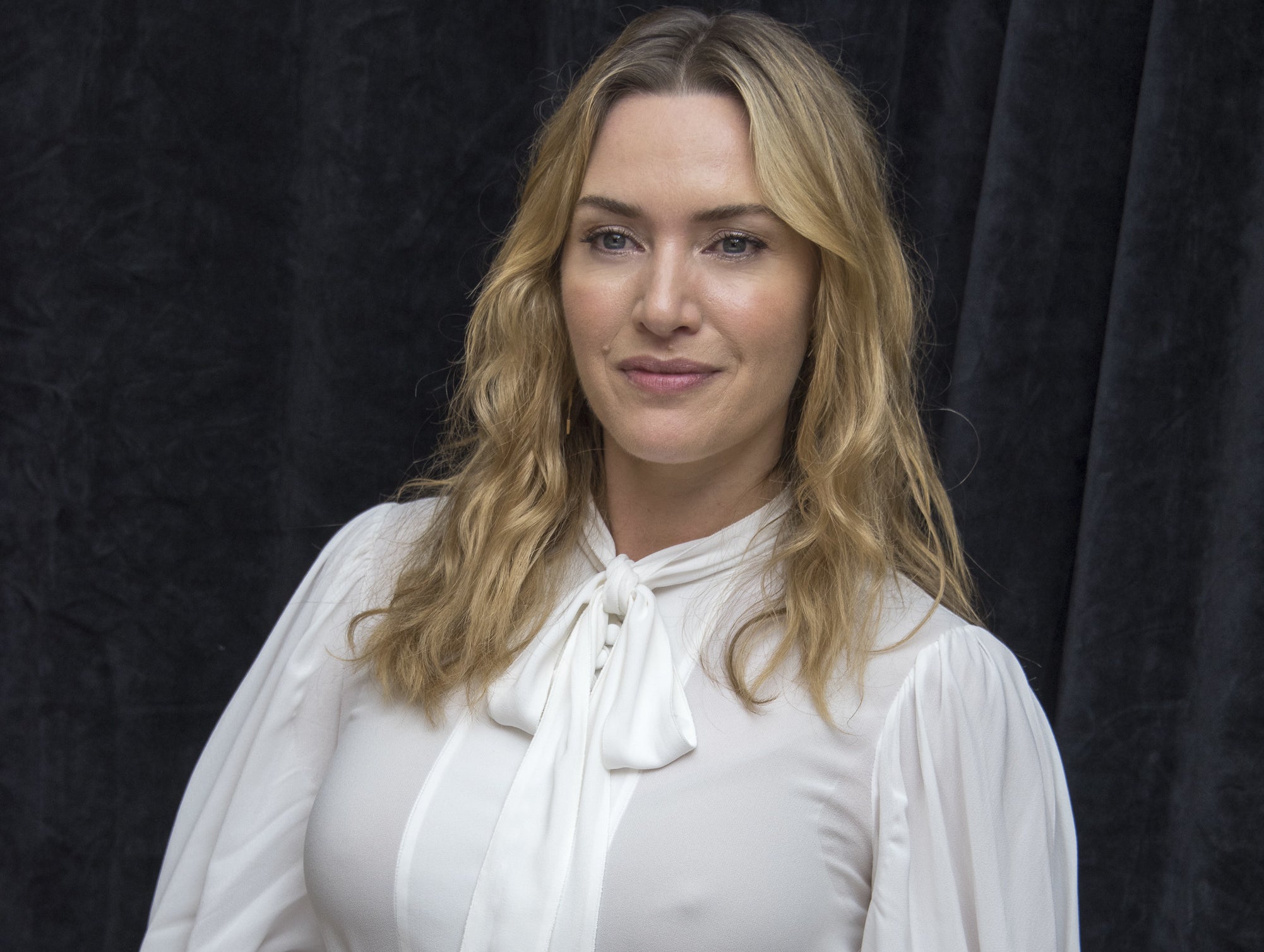 kate winslet wearing a white blouse with her hair down again a black backdrop