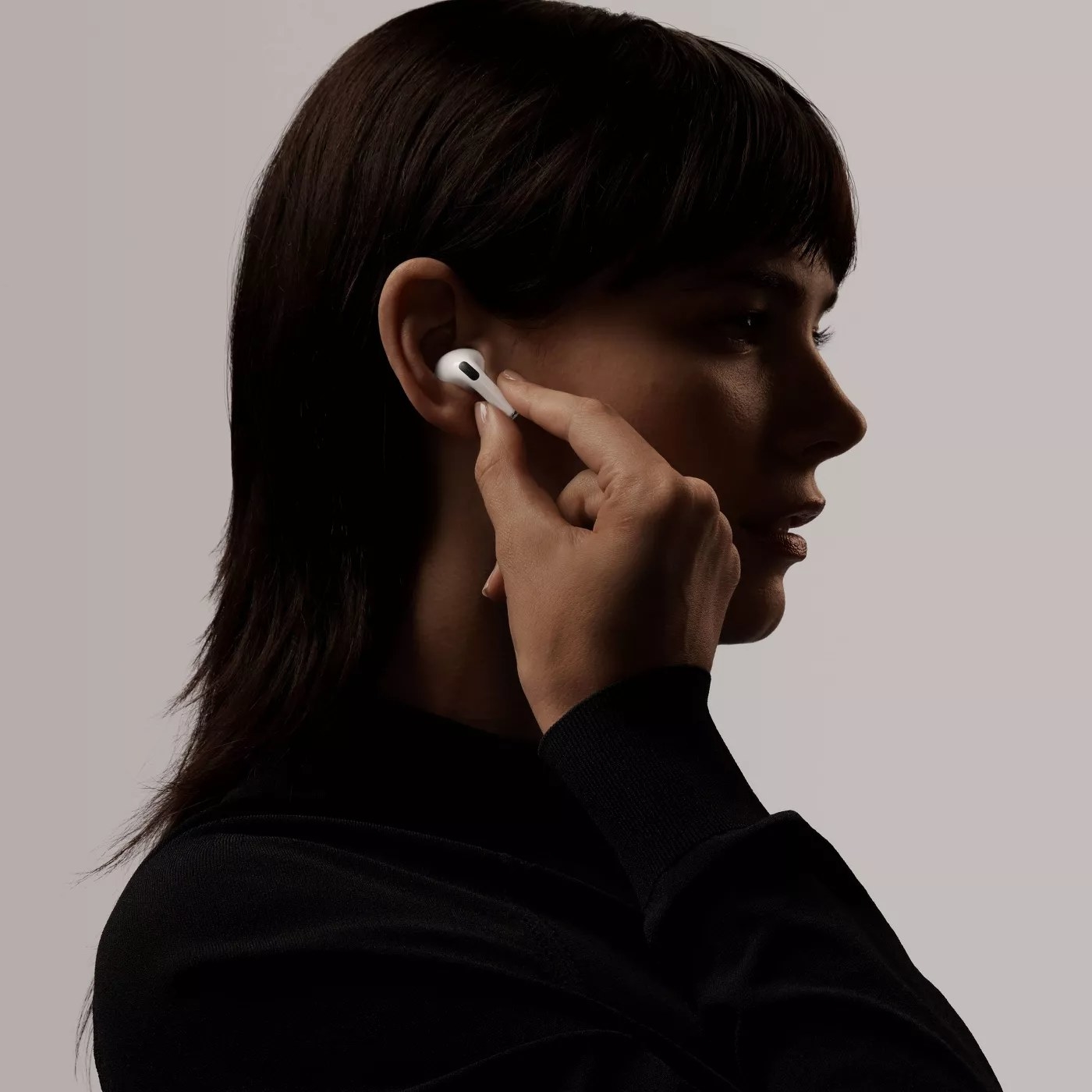 A side profile view of a model placing an Airpod in their ear
