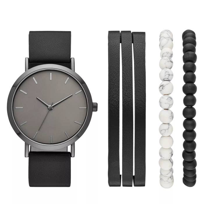 The set with a gray watch on a back faux leather strap, pictured beside a black faux leather bracelet, a white beaded bracelet, and a black beaded bracelet