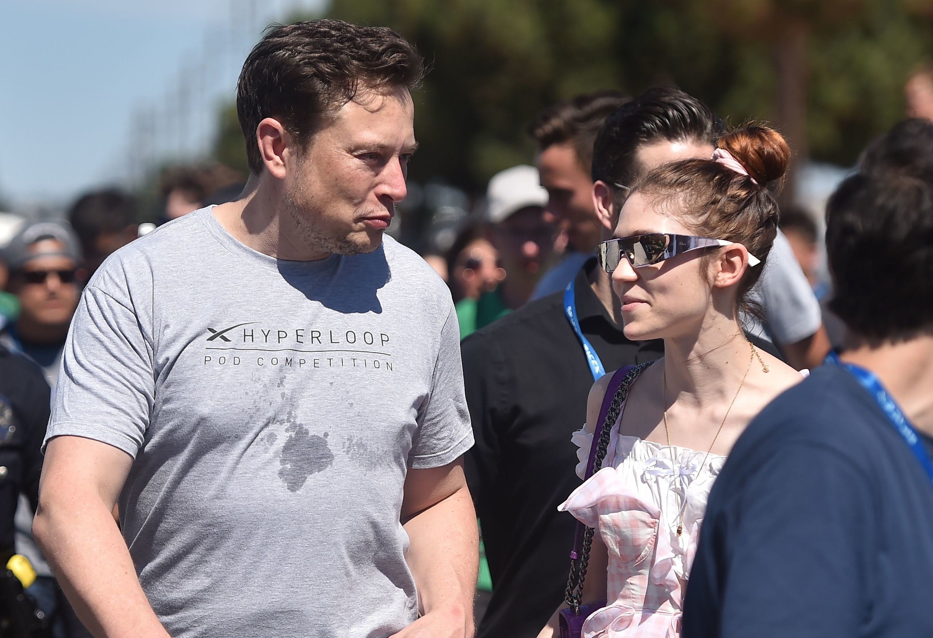 Elon Musk Grimes,穿着便服,看起来彼此过去参加过2018空间X Hyperloop Pod竞争在霍桑,加利福尼亚