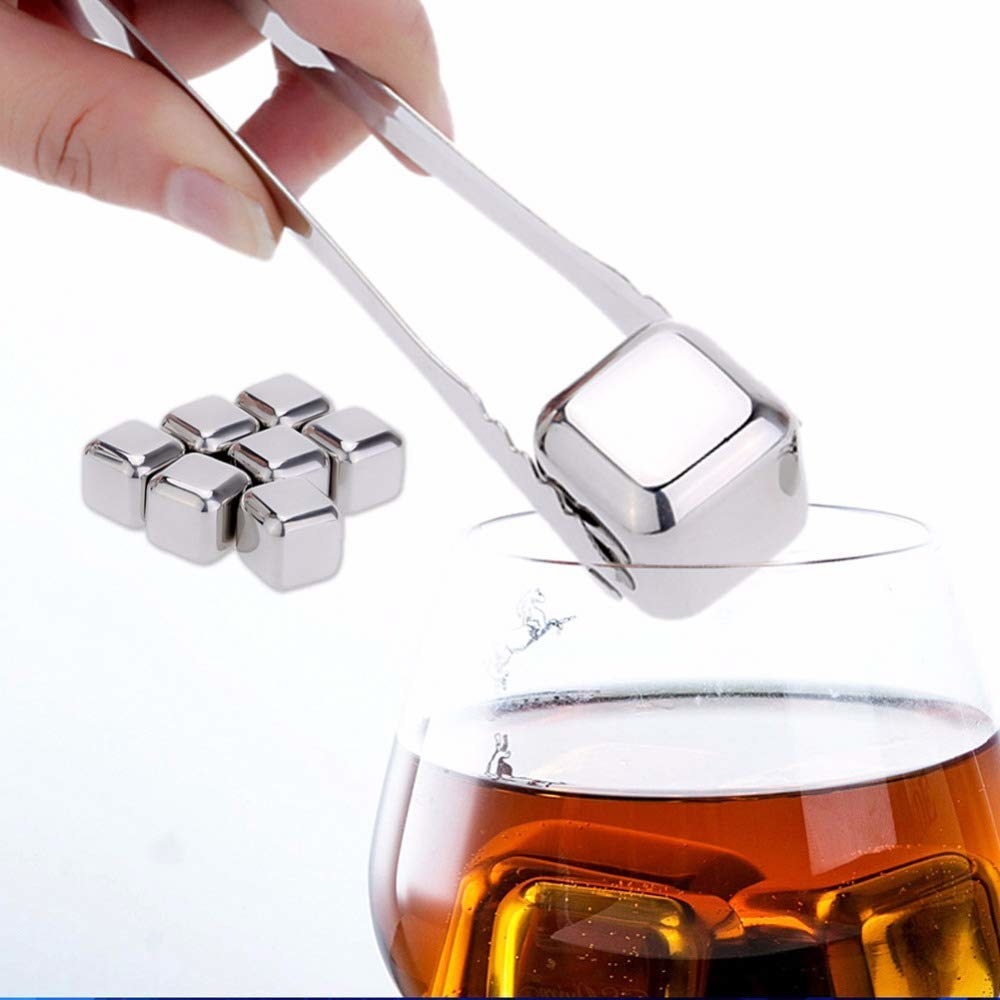 A person using tongs to add the reusable ice cube to a drink.