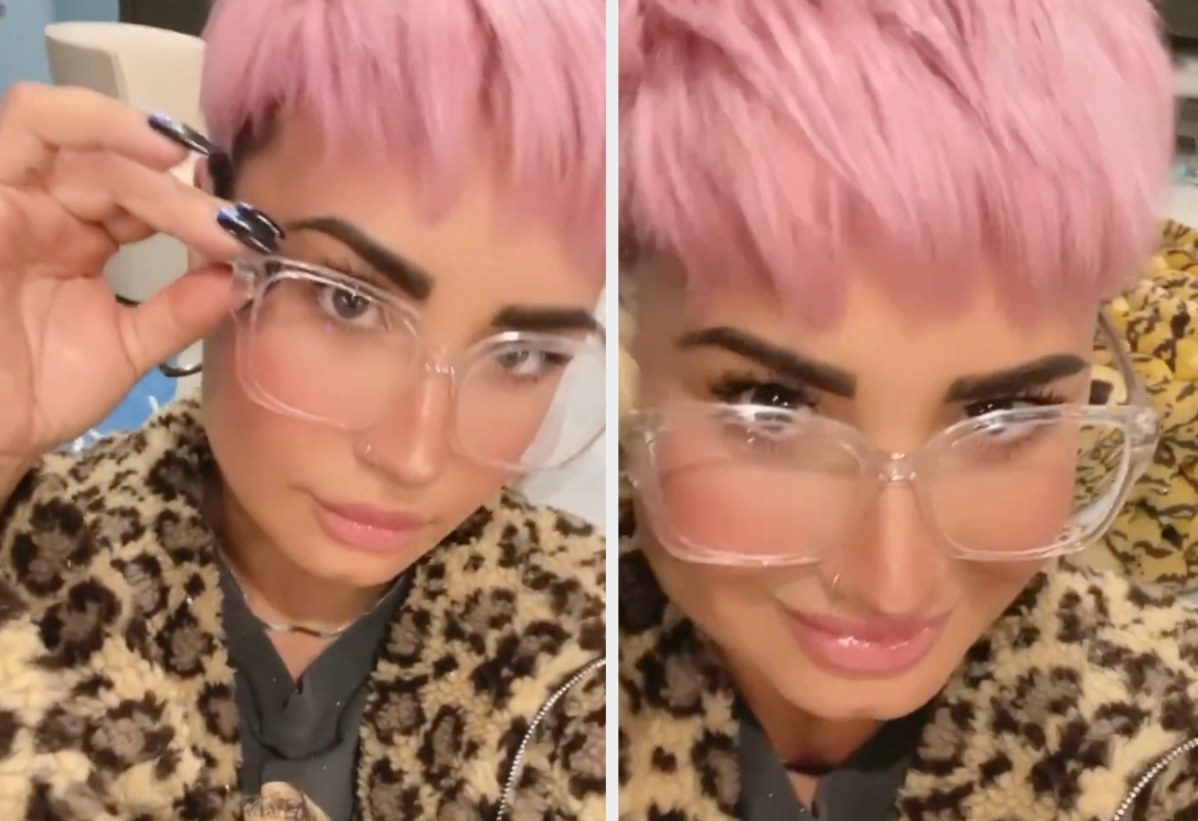 Demi Lovato taking a selfie video while wearing oversized glasses and pink hair