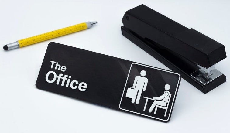 a black sign that says &quot;The Office&quot; sitting next to a pen and a stapler 
