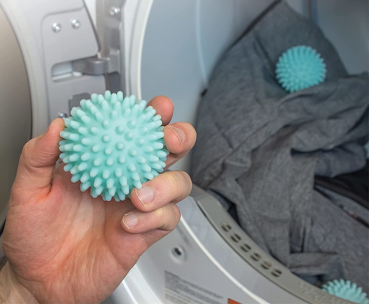 Someone holding up one of the spiky dryer balls; an open dryer is visible in the background